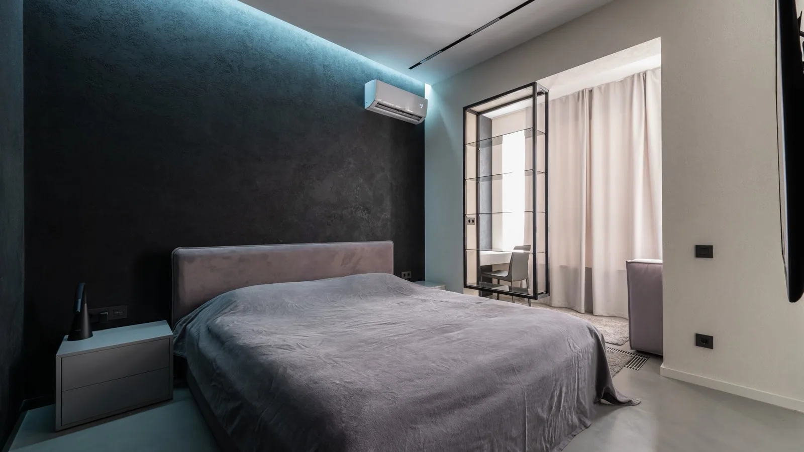 Dark modern bedroom with a white wall-mounted mini split indoor unit above the bed, the kind of single room a 12,000 BTU DIY mini split is sized for