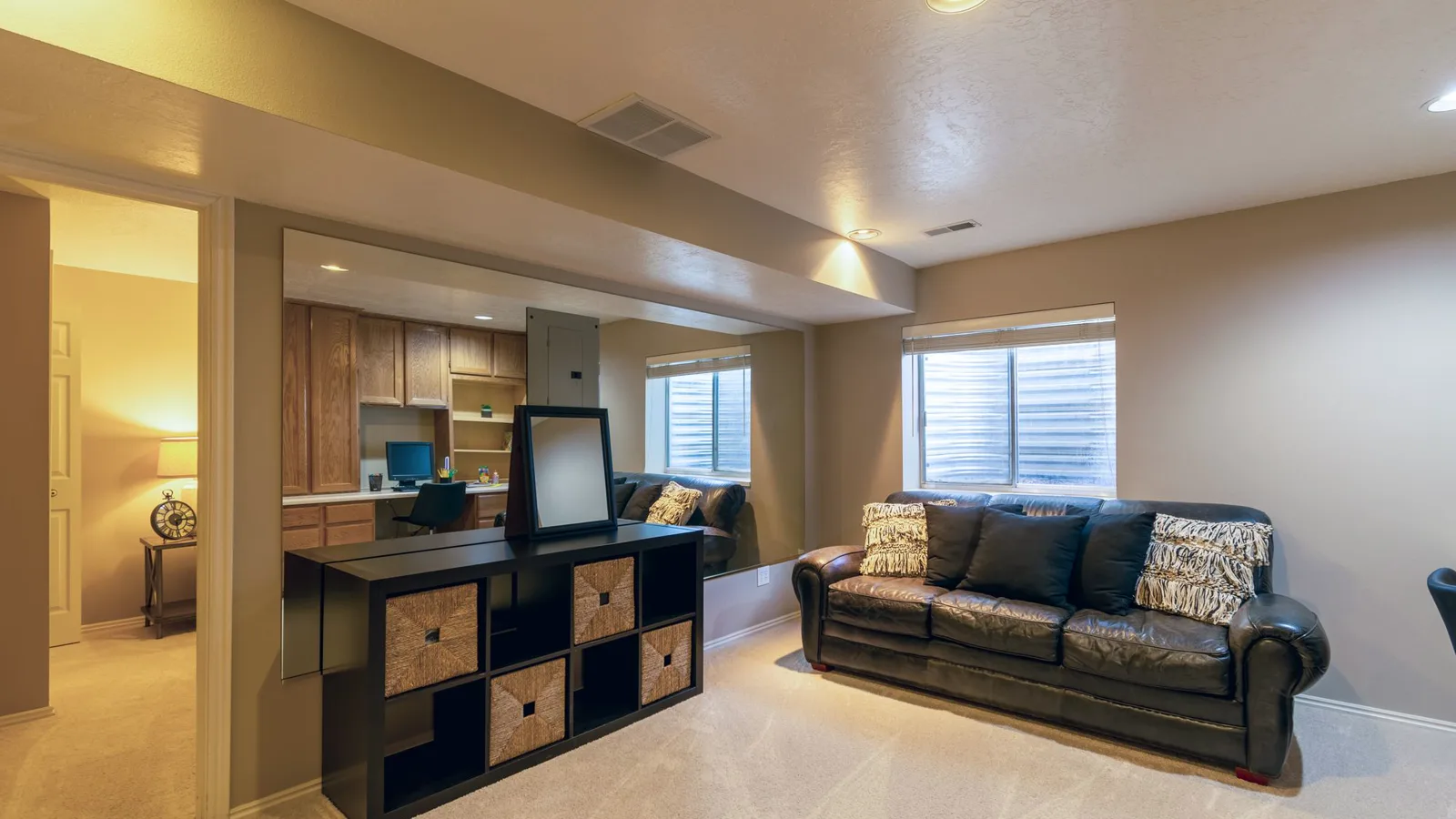 Finished basement family room with a leather sofa, carpet, a soffit and small daylight windows, the kind of below-grade space a basement DIY mini split heat pump has to heat and dehumidify