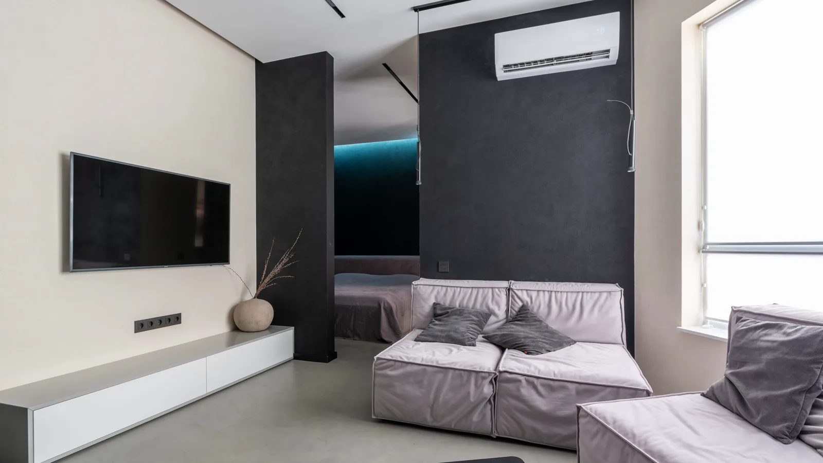 Ductless wall mounted heat pump head above a living room sofa, with a bedroom visible through the doorway, a typical two zone layout