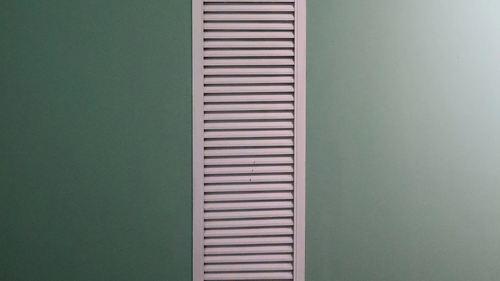 White louvered air grille set flush into a mint green wall, the only part of a DIY concealed duct mini split install you see in the finished room