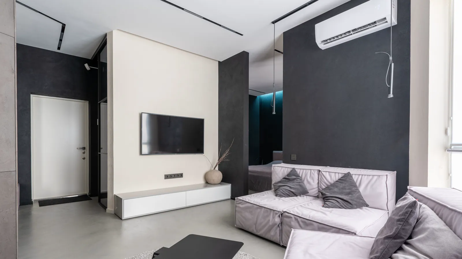 Wall mounted head of a dual zone mini split above a living room sofa, with a second room visible through the opening behind it