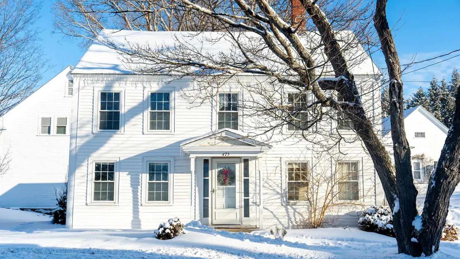 Two-story white house buried in snow on a sunny winter day, the kind of cold where a DIY mini split heat pump’s lowest heating temperature matters