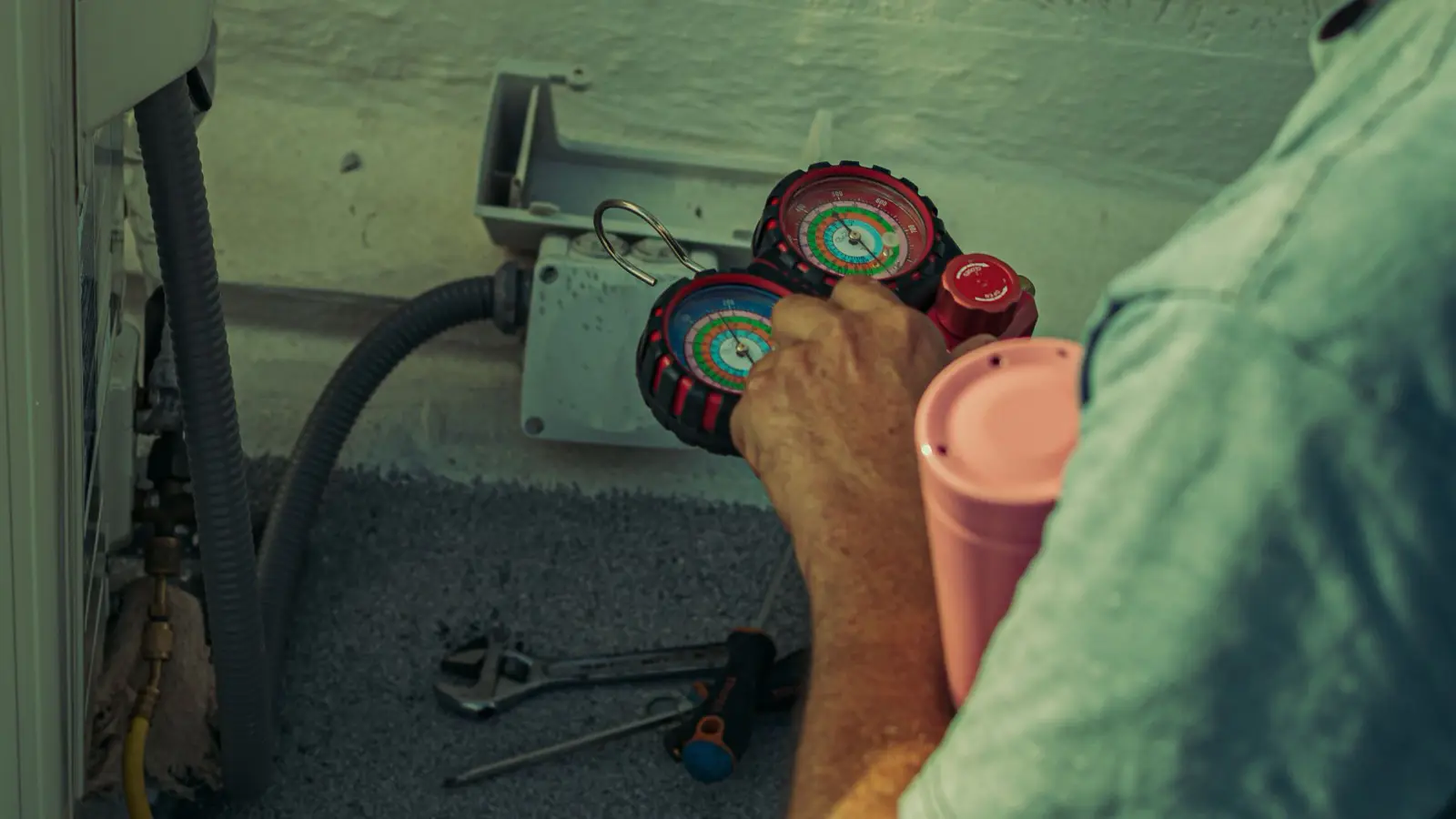 Technician holding a refrigerant manifold gauge set with a charging hose attached to a mini split outdoor unit's service port, the vacuum and gauge work a DIY pre-charged line set eliminates