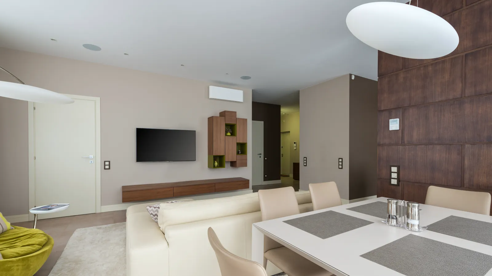 Slim white ductless indoor unit mounted high on a beige living room wall above a TV and wood shelves, the kind of head that needs regular mini split filter cleaning