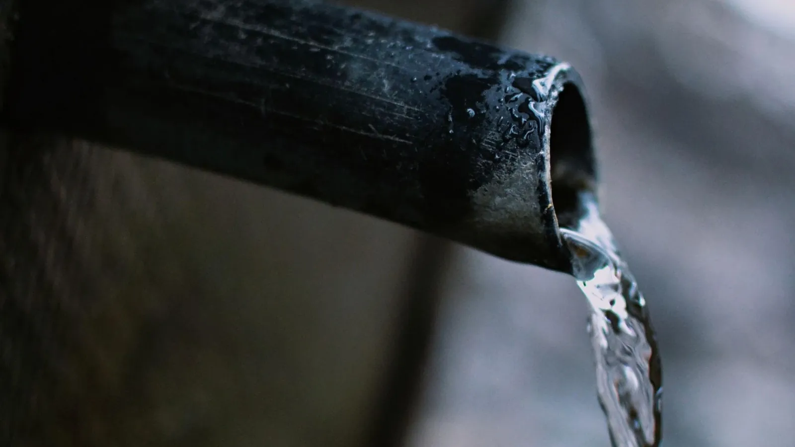 Water flows from a dark pipe with exterior moisture droplets, indicating a clogged mini split condensate drain