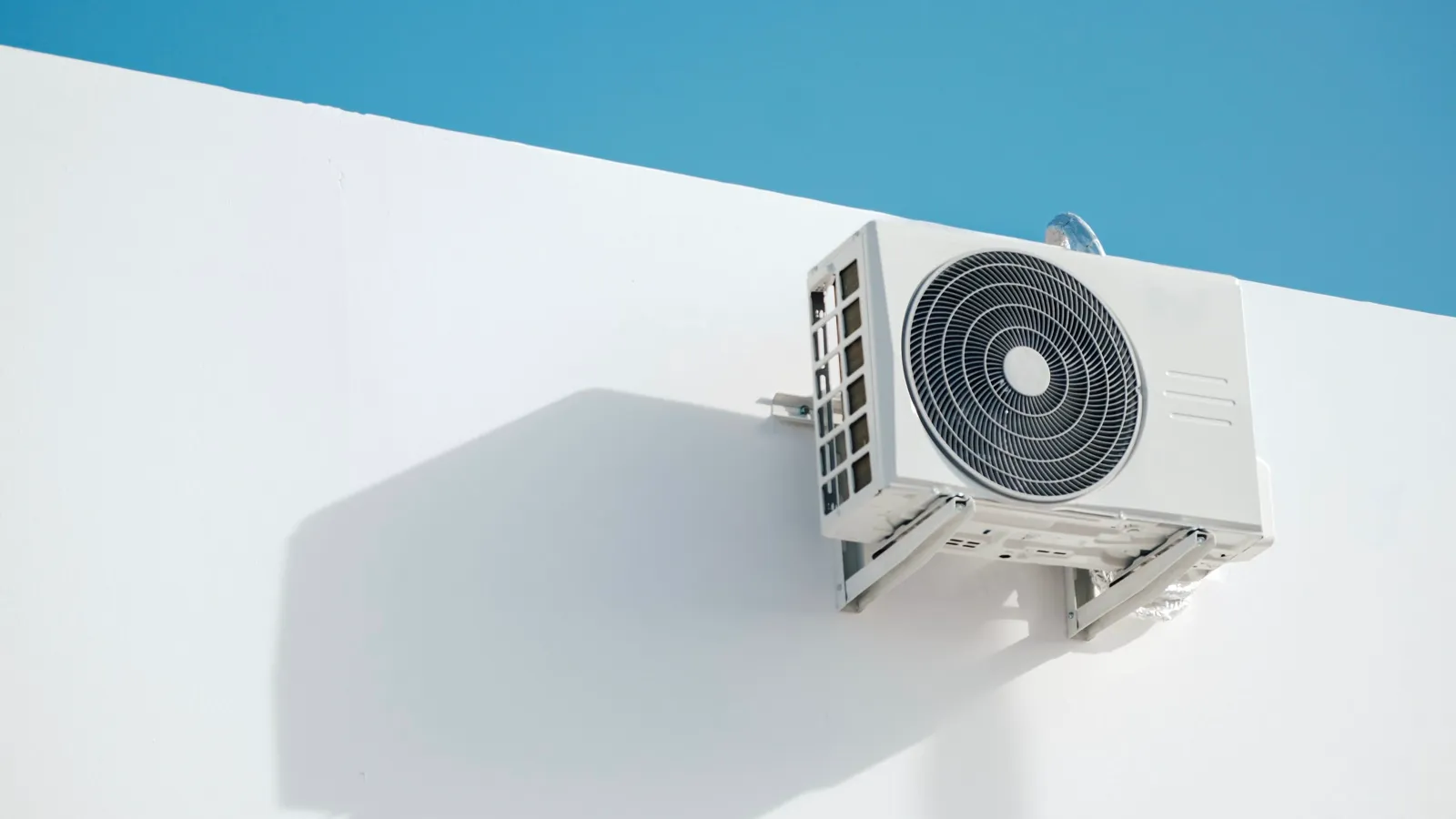 White mini split outdoor condenser on wall brackets under a clear blue sky, the kind of unit you size up when comparing MRCOOL DIY alternatives