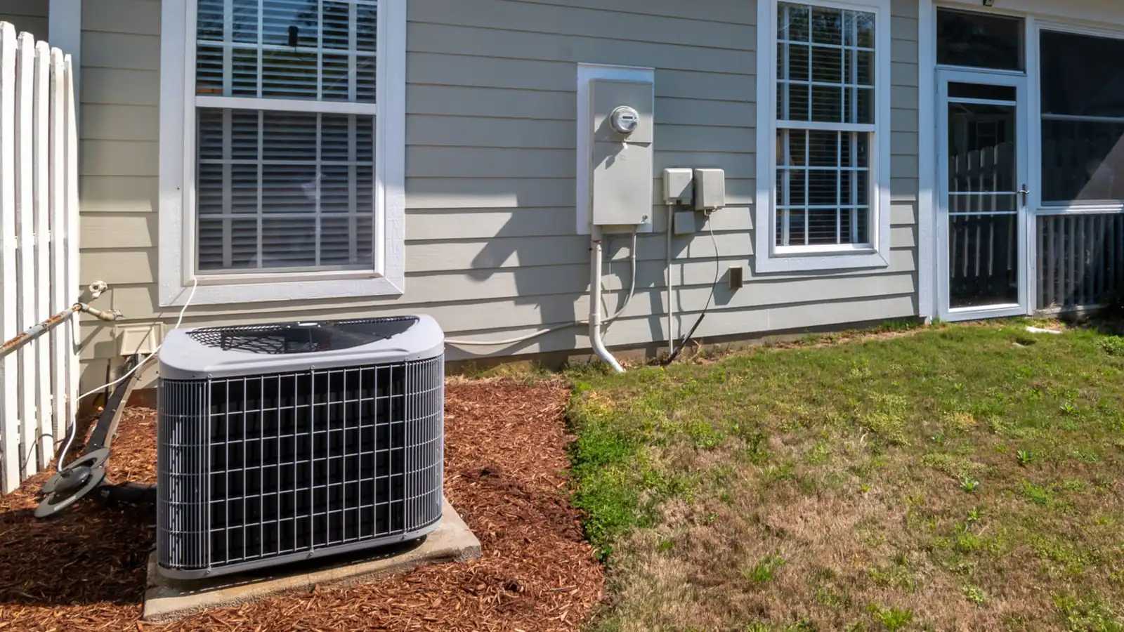 MRCOOL DIY 5th Gen 120V installation: outdoor heat pump condenser on a pad beside a house, with the electric meter, service disconnect box and conduit that feed its dedicated circuit
