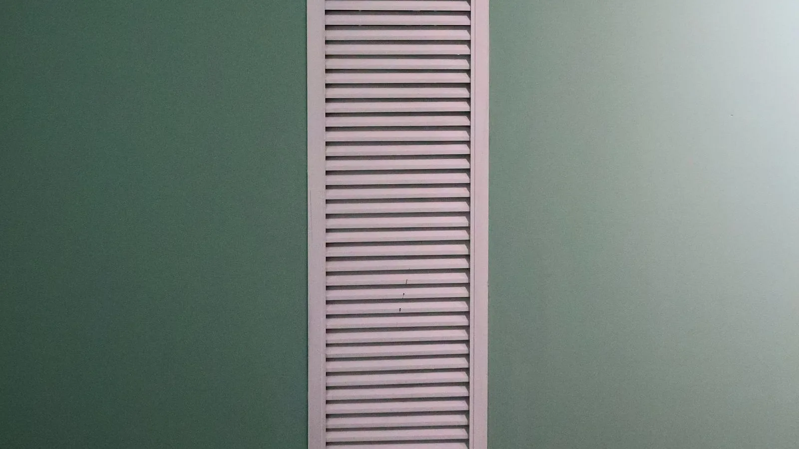 A tall white louvered return air grille set into a green painted wall